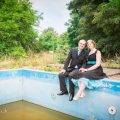 romantisch-stel-zittend-aan-rand-ruw-urbex-zwembad-in-tuin-vervallen-huis-met-pinupjurk-fotografie-door-ruwmantisch-nl-eline-kentie